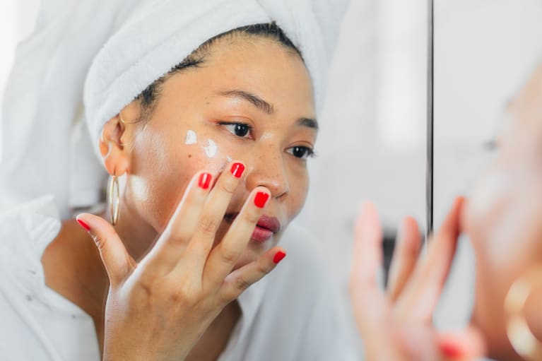 Woman Applying Moisturizer/Lotion in the Bathroom Mirror