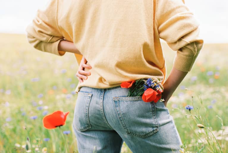 unrecognizable young woman from the back with a bouquet of wild flowers in a pocket of jeans