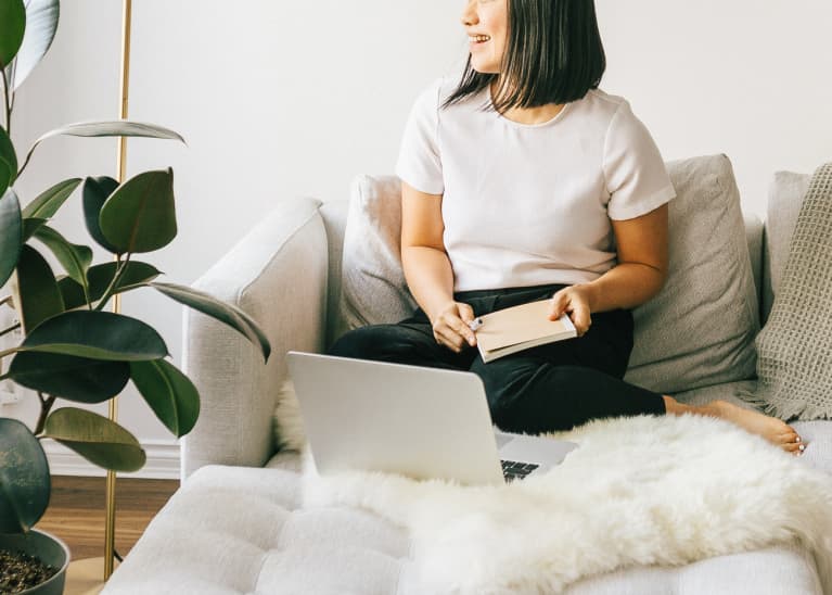 Woman Smiling on a Couch at Home with Her Laptop