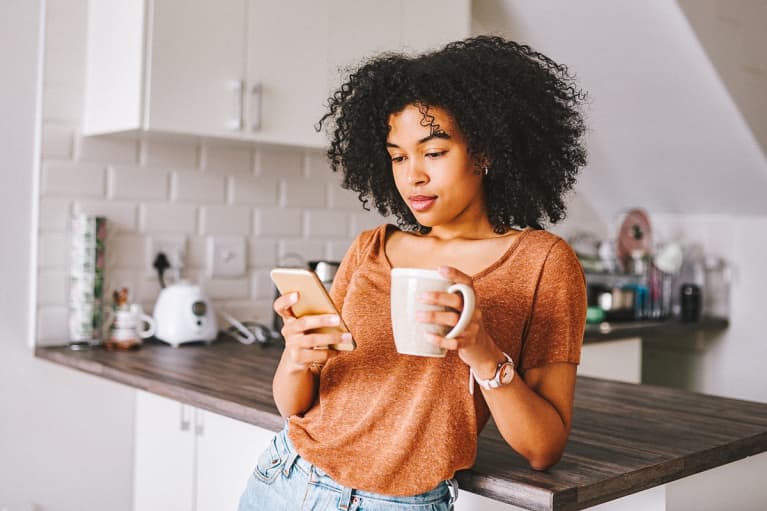 Young Woman Checking Her Phone In The Morning With a Cup of Coffee