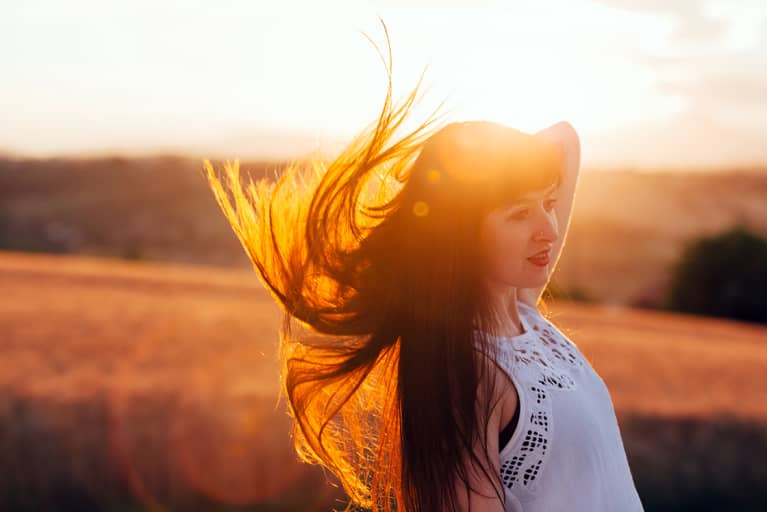 A Brunette Lady Flicks Her Hair Back, It Is Back Lit By The Sunset
