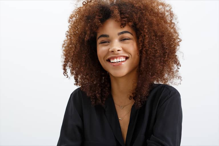 Black woman with curly brunette hair, smiling against a white background.