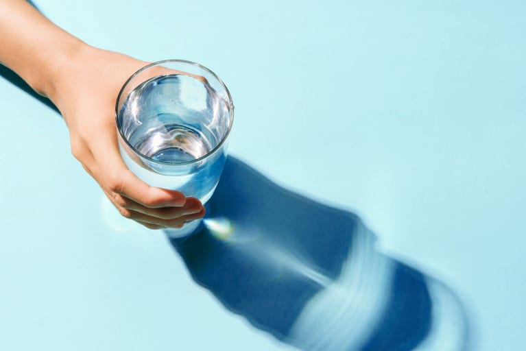 Hand holding water glass in strong lighting against minimal blue seamless