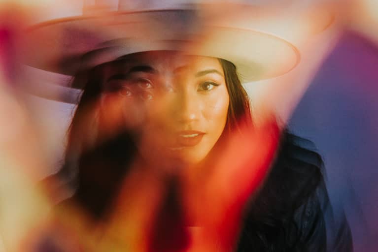 emale wearing wide brim hat poses for portrait shot through a prism. Colorful abstract prismatic portrait.