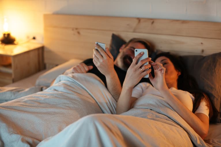 Couple In Bed Before Going to Sleep, Both Looking At Their Phones
