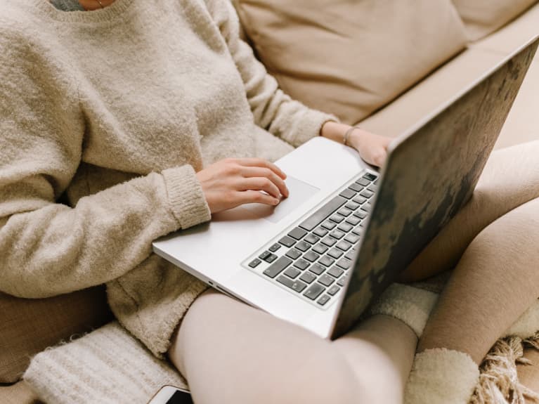 Anonymous Woman In Sweater Using Laptop On Sofa