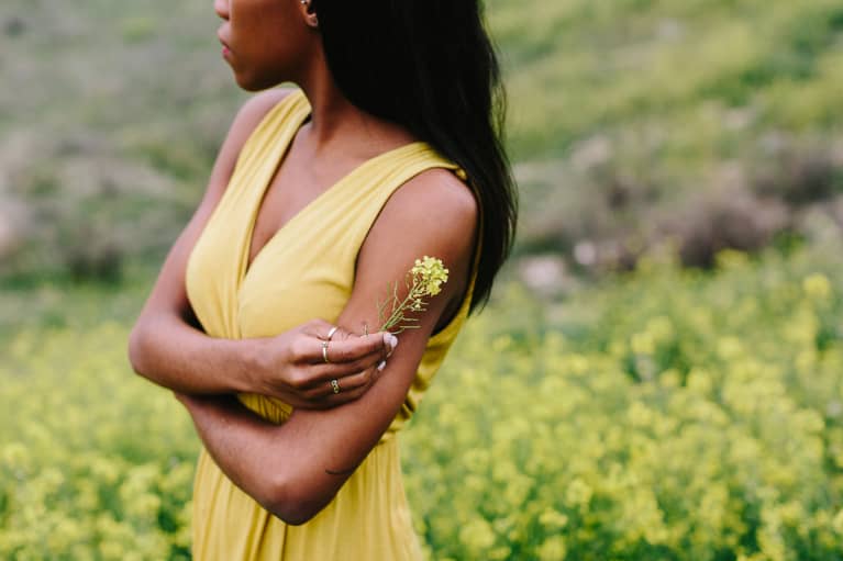 Detail shot of a Black woman holding a yellow flower in a flowery field
