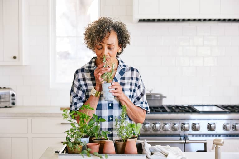 Senior Woman smelling fresh herbs in her kitchen in pots that she planted