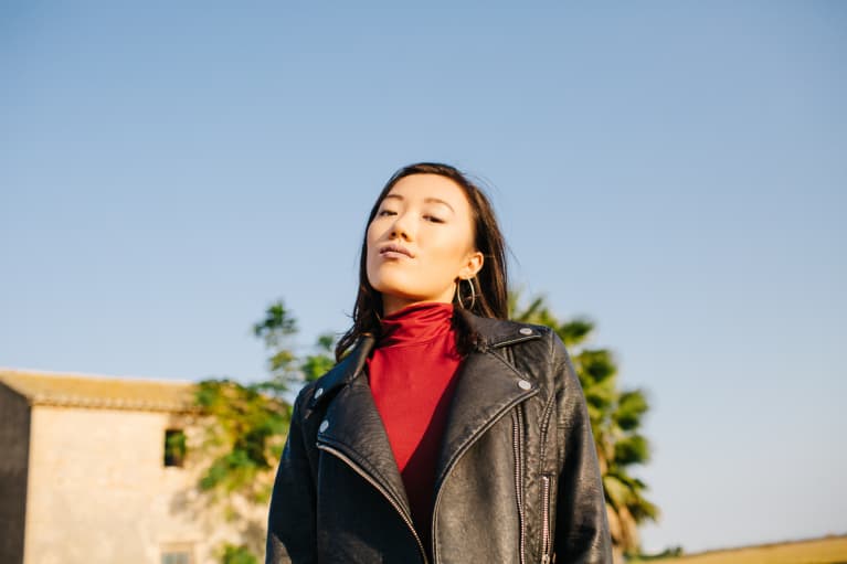 Portrait of stylish young woman in black jacket looking confidently at camera on rural background.